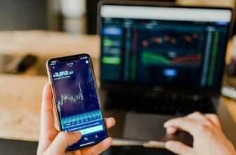 hand holidng phone with laptop in background showing forex chart