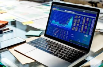 laptop on glass desk with papers showing trading chart