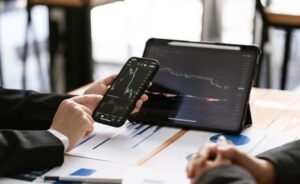 man holding phone with tablet both showing trading chart
